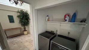 Eine kleine Küche mit zwei Edelstahlgeräten, einer Topfpflanze und einem Regal mit Reinigungsmitteln.