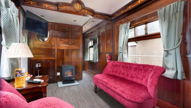 Ein gemütliches Zimmer mit einem roten Sofa, einem Kamin, einem Fernseher und einem Tisch mit Lampe und Buch.