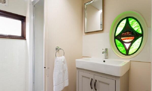 A bathroom with a white sink, a mirror, and a green stained glass window.