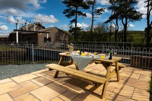 An outdoor dining area with picnic tables, a fence, and a building in the background.