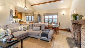 A cozy living room with a sectional sofa, a dining table with chairs, a fireplace, and a kitchen in the background. - 3 Bed in Upottery (oc-t28828) (Upottery)