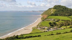 A coastal landscape with a beach, a small village, and a hill with dense vegetation. - 3 Bed in Upottery (oc-t28828) (Upottery)