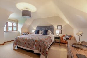 A spacious attic bedroom with a large bed, a nightstand, a chair, and a vanity with a mirror. - 3 Bed in Upottery (oc-t28827) (Upottery)
