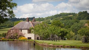 A stone house with a pond in front, surrounded by greenery and hills. - 3 Bed in Upottery (oc-t28827) (Upottery)