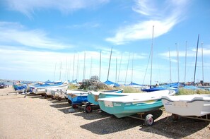 Eine Reihe kleiner Boote liegt auf einem Kiesstrand bei blauem Himmel.