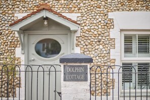 Ein verschlossenes Eingangstor mit einem Schild, auf dem 'DOLPHIN COTTAGE' steht, vor einem Gebäude mit einer Steinauffassung.