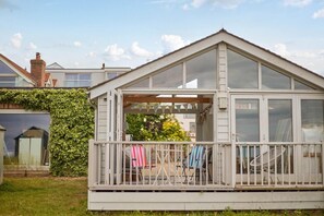 Ein kleines, eingeschossiges Haus mit Balkon, überdachter Veranda und Garten.