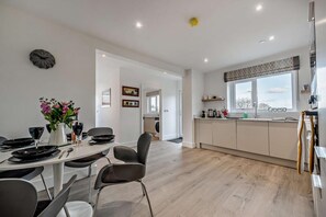 Une cuisine moderne avec une fenêtre, un coin repas avec une table dressée pour quatre personnes, et un couloir menant à une autre pièce.