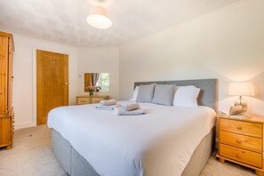 A bedroom with a large bed, a wooden wardrobe, a bedside table with a lamp, and a window with curtains. - 3 Bed in Goldsithney (oc-b28811) (Goldsithney)
