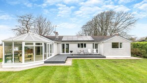 Et moderne hus med et solrum, en terrasse med udendørs møbler og en velplejet græsplæne.