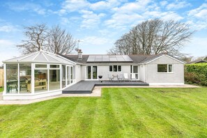 Une maison moderne dotée d’une véranda, d’un patio avec mobilier d’extérieur et d’une pelouse bien entretenue.