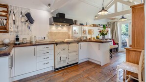 Een moderne keuken met witte kasten, houten aanrecht en een centraal eiland. Er zijn hangende keukengerei, een koffieapparaat en een fornuis.
