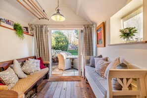 A cozy living room with a sofa and a bench, a dining table, and a view of the garden through a glass door. - 2 Bed in Langham (oc-t28836) (Langham)