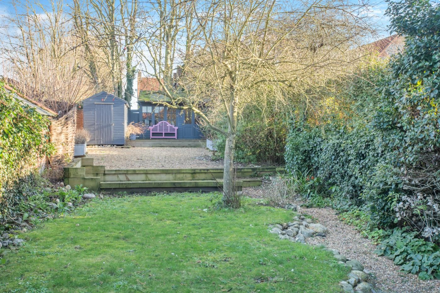 A backyard with a wooden deck, a shed, and a bench.
