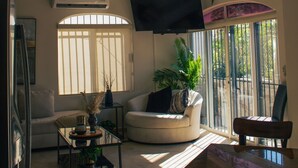 Una sala de estar con ventilador de techo, televisor de pantalla plana, sofá, mesa de centro y mesa de comedor.