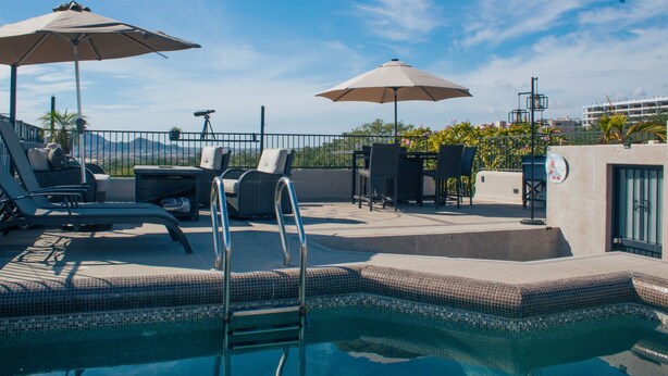Un área de piscina en la azotea con sillones, sombrillas y vistas a las montañas.