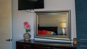 Un dormitorio con un aparador, un televisor montado en la pared, un espejo y una puerta.