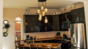 Una cocina moderna con armarios oscuros, un refrigerador de acero inoxidable y una isla central con taburetes de bar.