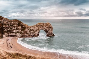 A coastal landscape with a natural rock arch formation, a sandy beach, and the ocean. - 4 Bed in Wool (oc-p28895) (Wool)