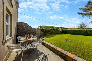 Een terras met een tafel en stoelen, een stenen muur en een verzorgd gazon.