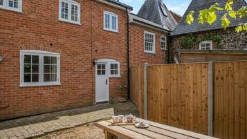 A brick house with a wooden fence, a door, and a picnic table with cups and a teapot.