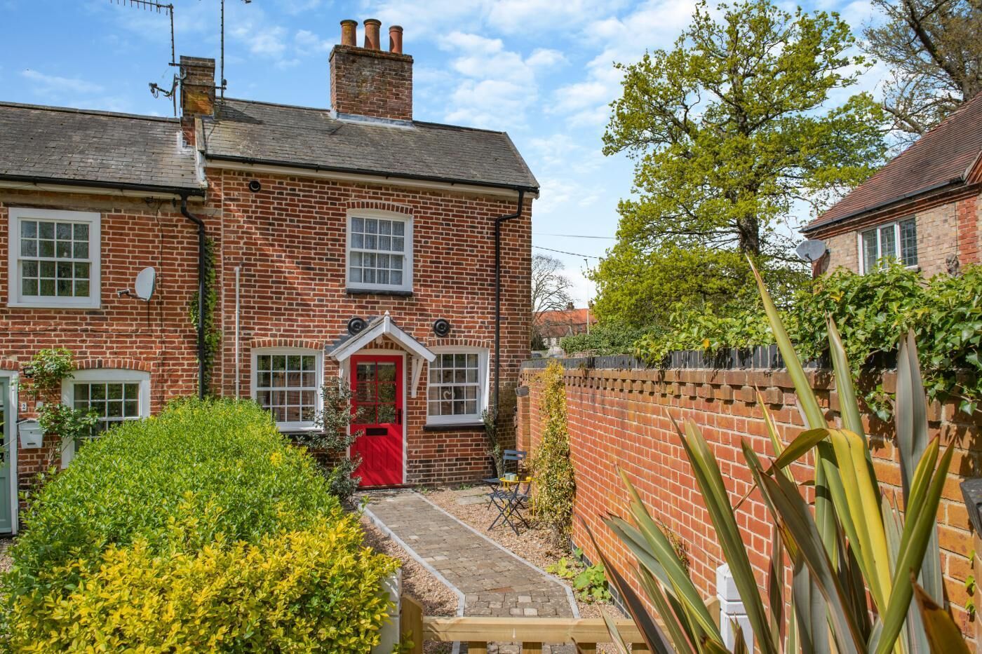 A brick house with a red door, a small garden, and a brick wall.