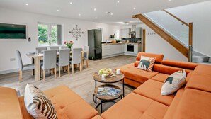 A modern living room with a sofa, coffee table, and dining area. - 4 Bed in Retorrick Mill (oc-t28899) (Saint Mawgan)