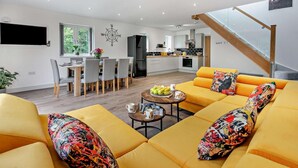 A modern living room with a yellow sofa set, a dining area with a wooden table, and a kitchen in the background. - 4 Bed in Retorrick Mill (oc-w28897) (Saint Mawgan)
