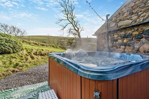 Ein Whirlpool im Freien mit einer Steinwand und einer grünen Landschaft im Hintergrund.