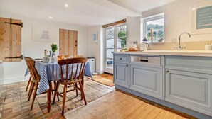A modern kitchen with a dining area, featuring a wooden table, chairs, and a view of the outdoors. - 3 Bed in Dunwich (oc-l18684) (Dunwich)