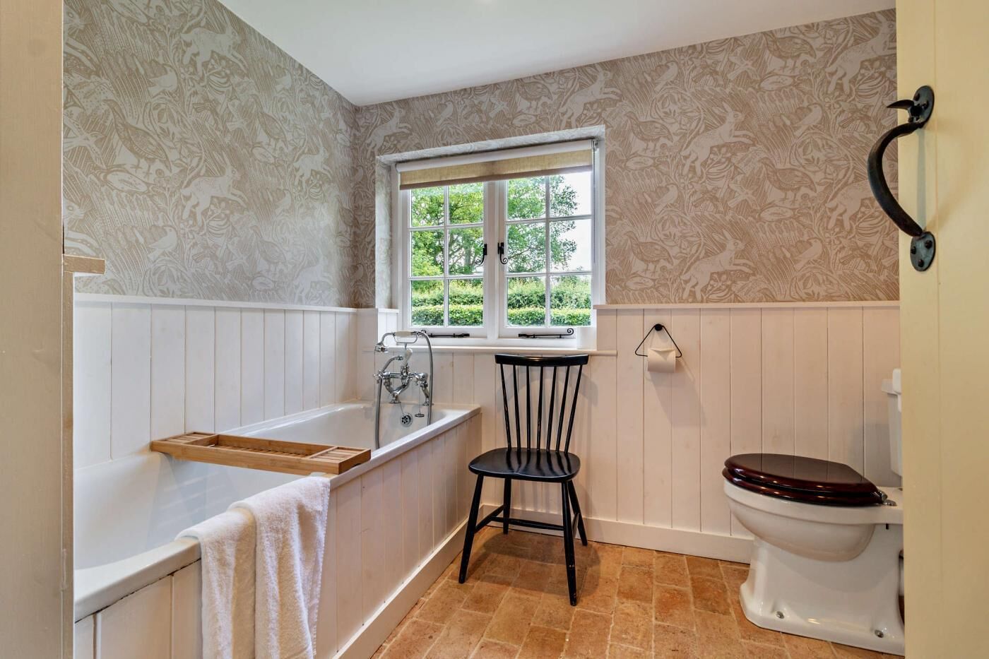 Ein Badezimmer mit Badewanne, Toilette, Fenster und Stuhl.