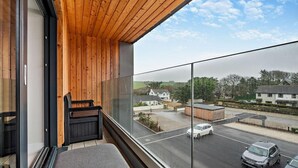 A balcony with a wooden ceiling, a bench, and a view of a residential area with houses and cars. - 2 Bed in Harlyn Bay (oc-s28921) (Harlyn Bay)
