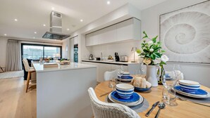 A modern kitchen with a central island, dining area with blue and white plates, and a large abstract painting on the wall. - 2 Bed in Harlyn Bay (oc-s28921) (Harlyn Bay)