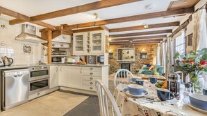 Una cucina con travi in legno, elettrodomestici in acciaio inossidabile e un'area pranzo con tavolo imbandito per quattro persone.