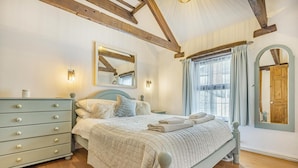 Una camera da letto con un letto, una cassettiera, uno specchio e travi in legno al soffitto.