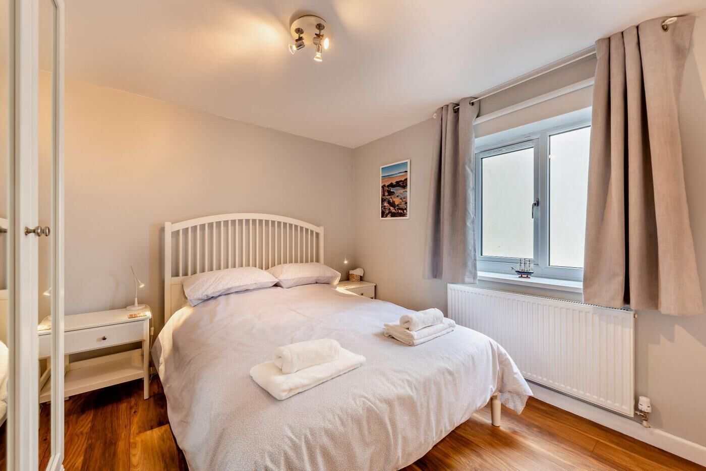 Ein Schlafzimmer mit Bett, Nachttischen, einem Fenster mit Vorhängen und einer Heizung.