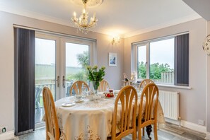 Une salle à manger avec une table dressée pour six personnes, un lustre et une vue sur l’extérieur.