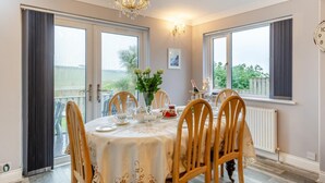 Een eetkamer met een gedekte tafel voor zes personen, een kroonluchter en uitzicht op het omliggende landschap.