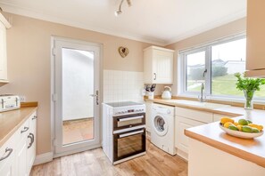 A modern kitchen with a built-in oven, a washing machine, and a window with a view of the outdoors. - 3 Bed in Hope Cove (oc-hocov) (Hope Cove)