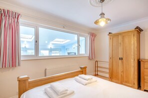 A bedroom with a large bed, a wooden wardrobe, a radiator, and a window with curtains. - 3 Bed in Hope Cove (oc-hocov) (Hope Cove)
