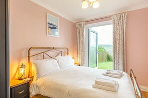 Une chambre à coucher comprenant un lit, une table de chevet, une lampe, une fenêtre avec des rideaux et une vue sur l’extérieur.