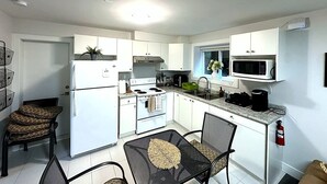 A compact kitchen with white cabinets, a stove, microwave, and a sink. There are two chairs and a small dining table. - Charming 2 BR 1BA Basement suit in White Rock with WiFi (White Rock)