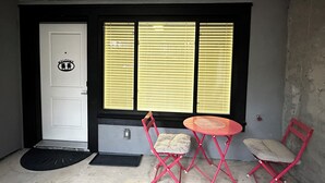 A room with a white door, three windows with blinds, a small red table, and two red chairs. - Charming 2 BR 1BA Basement suit in White Rock with WiFi (White Rock)