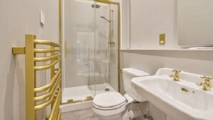 Un baño moderno con ducha de vidrio, inodoro blanco y lavamanos con detalles dorados.