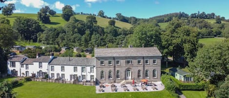 A large, historic building with a courtyard, surrounded by lush green hills and trees.