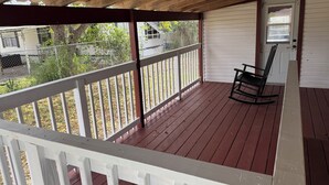 Eine überdachte Veranda mit weißer Holzvertäfelung, einem Schaukelstuhl und einer Tür mit Fenster.
