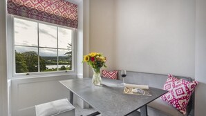 Een eetgedeelte met een tafel, een bank en uitzicht op de omgeving door een raam.