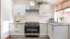 Une cuisine moderne avec des armoires blanches, une hotte de cuisinière en acier inoxydable, un four et une fenêtre équipée de stores.