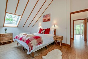A bedroom with a sloped ceiling, wooden beams, a large window, a bed with red pillows, bedside tables, and a view to the outside. - 4 Bed in Rhayader (oc-m28919) (Nantmel)