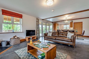 A spacious living room with a leather sofa, a television, and a coffee table with board games. - 4 Bed in Rhayader (oc-m28919) (Nantmel)